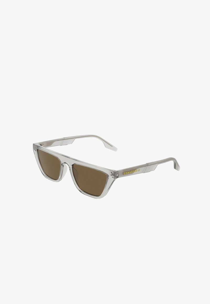 Lunettes de soleil en plastique transparent avec des verres teintés marron, forme angulaire, et logo "Converse" doré sur les branches. Design élégant et léger.