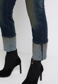 Mörkblå denimjeans med ljusblå uppvikning, med rå nederkant och synlig sömnad. Parat med svarta mockastövlar med dragkedjor.