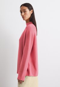 Roze coltrui met lange mouwen, met een ontspannen pasvorm en ribbeltextuur. Gecombineerd met een lichtbeige onderstuk.