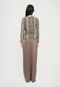 Long-sleeve top with a beige and black snake print pattern paired with high-waisted, wide-leg brown trousers, featuring a smooth texture.