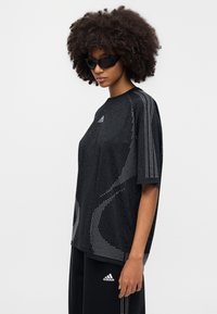 Camiseta deportiva negra de manga corta, con un diseño perforado y detalles reflectantes. Logo visible en el pecho.