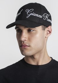 Svart basebollkeps med böjd skärm och broderad vit text. Släta tyg, strukturerad form, bärs med en enkel svart t-shirt.