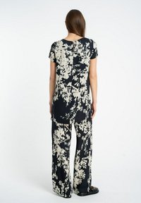 Dwuczęściowy strój w kwiatowy wzór, składający się z bluzki z krótkim rękawem i spodni o szerokich nogawkach. Kolory obejmują czerń i krem; miękka tkanina o gładkiej fakturze.