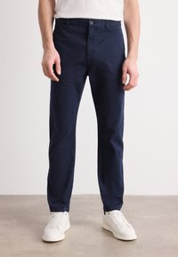 Marineblauwe katoen chinos met een rechte pasvorm, voorzien van een knoopsluiting en zakken aan de voorkant, gecombineerd met witte sneakers. Soepele textuur.