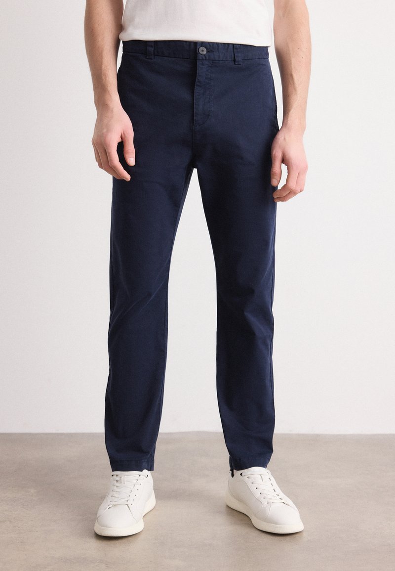 Marineblauwe katoen chinos met een rechte pasvorm, voorzien van een knoopsluiting en zakken aan de voorkant, gecombineerd met witte sneakers. Soepele textuur.