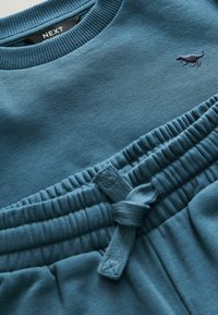 Tolle Sweatshirt in teal und passende Jogginghosen; der Stoff ist weich mit gerippten Bündchen und Bund. Beinhaltet ein kleines, gesticktes Logo eines Hundes.