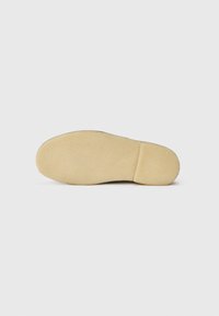 Shoe sole with a smooth, beige rubber bottom showing slight texture; rounded shape with a flat heel and minimal design details.