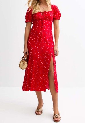 Rød prikprikket kjole med pufærmer, hjerteformet udskæring og sideslidse. Båret med en rund flettet taske og sandaler med stropper.