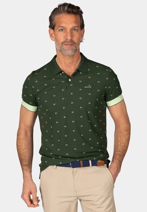 Donkergroene polo met kleine witte patronen, met een placket met twee knopen en contrasterende lichtgroene manchetten. Draag het met een beige broek en een marineblauw riem.