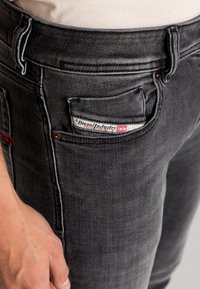 Vaqueros de denim negro con un diseño ajustado, que cuentan con un pequeño bolsillo frontal, acentos de costura roja y una etiqueta visible de Diesel Industries.
