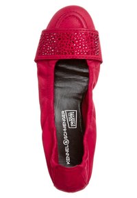 Ballerines en cuir rouge avec un bout arrondi, ornées d'une bande cloutée. Texture lisse avec un intérieur noir. Nom de la marque visible à l'intérieur.