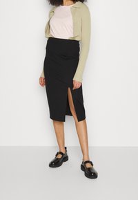 Gonna nera a matita con uno spacco laterale, abbinata a un top rosa chiaro e a un cardigan verde chiaro. Scarpe nere con una suola spessa completano il look.