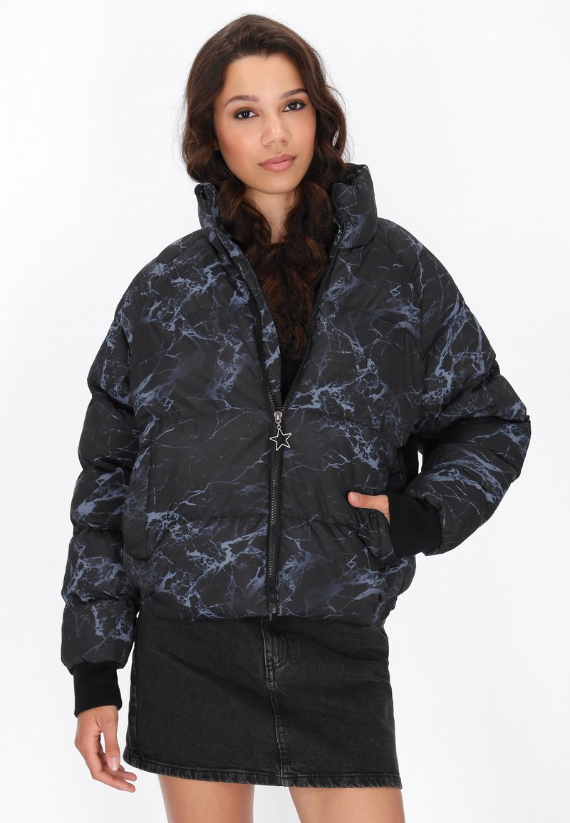 Zwarte gewatteerde jas met een marmerpatroon in blauw. Heeft een hoge kraag, ritssluiting en geribbelde manchetten. Gemaakt over een zwarte denim rok.