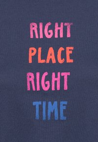 Camiseta azul marino con un texto audaz y multicolor: "LUGAR CORRECTO" en naranja y rosa, "MOMENTO CORRECTO" en azul, todo con un acabado texturizado.