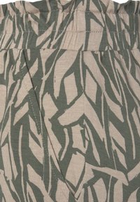 Elastic-waisted pants in beige fabric featuring a green abstract leaf pattern. The texture is smooth with visible stitching along seams.