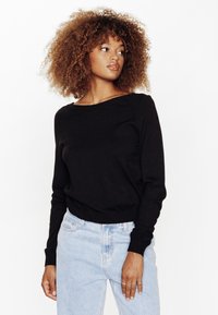 Maglione nero a maglia con scollo a barca e maniche lunghe, abbinato a jeans a vita alta di colore blu chiaro, esposto su uno sfondo bianco.