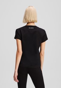 Juodas medvilninis T-shirt su trumpomis rankovėmis, apvaliu kaklu ir baltu "KARL LAGERFELD" logotipu gale. Lygus audinys, laisvas siluetas.