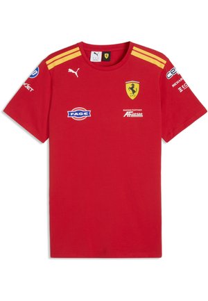 Czerwona koszulka wyścigowa Ferrari z krótkim rękawem, żółtymi paskami na ramionach, logo Puma, herbem Ferrari oraz wieloma logo sponsorów na piersi i rękawach.