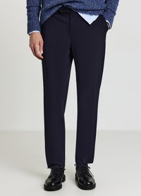 Pantalon bleu marine en tissu lisse avec une coupe droite, doté d'une ceinture et de poches avant. Associé à des chaussures noires.