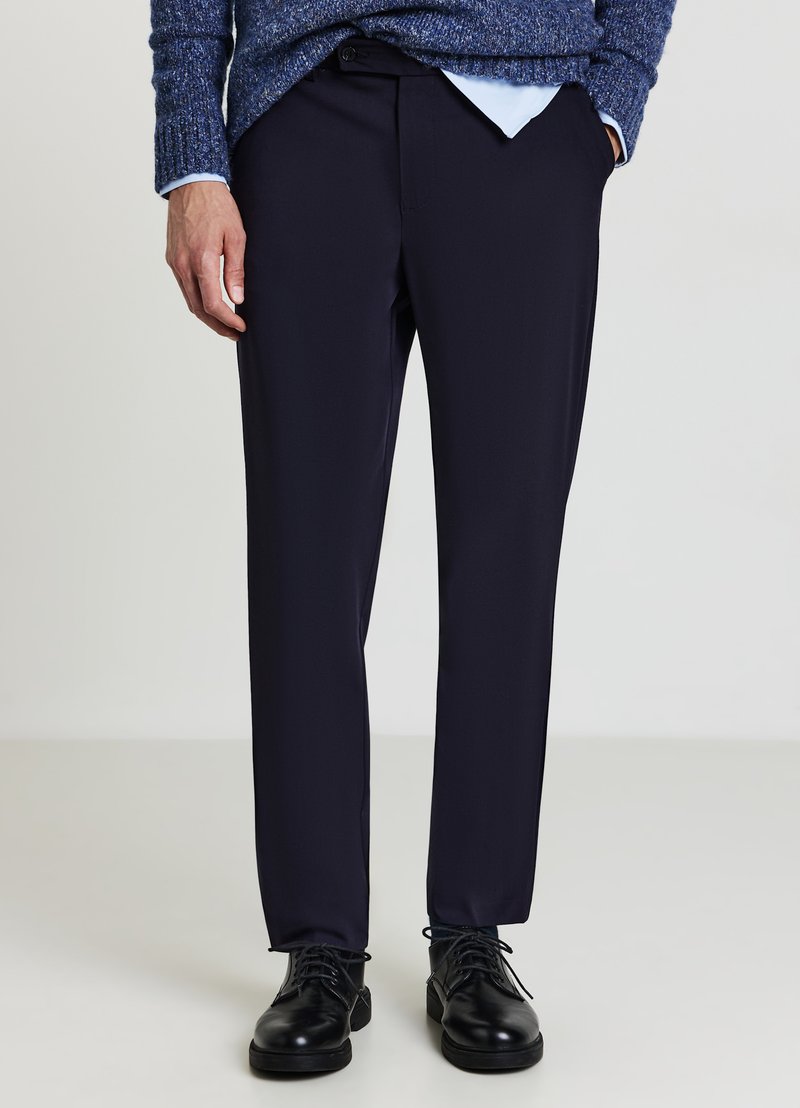 Pantalon bleu marine en tissu lisse avec une coupe droite, doté d'une ceinture et de poches avant. Associé à des chaussures noires.