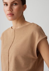 Beige gebreide top met een ronde halslijn, korte mouwen en een nette naaddetail aan de voorkant. Zachte textuur en lichtgewicht stof.