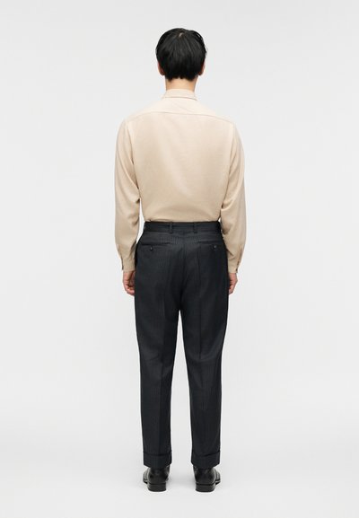 Μπεζ πουκάμισο με μακριά μανίκια συνδυασμένο με σκούρο παντελόνι με ριγέ. Το παντελόνι διαθέτει δύο πίσω τσέπες και ρεβέρ στο τελείωμα. Μαύρα παπούτσια ολοκληρώνουν την εμφάνιση.