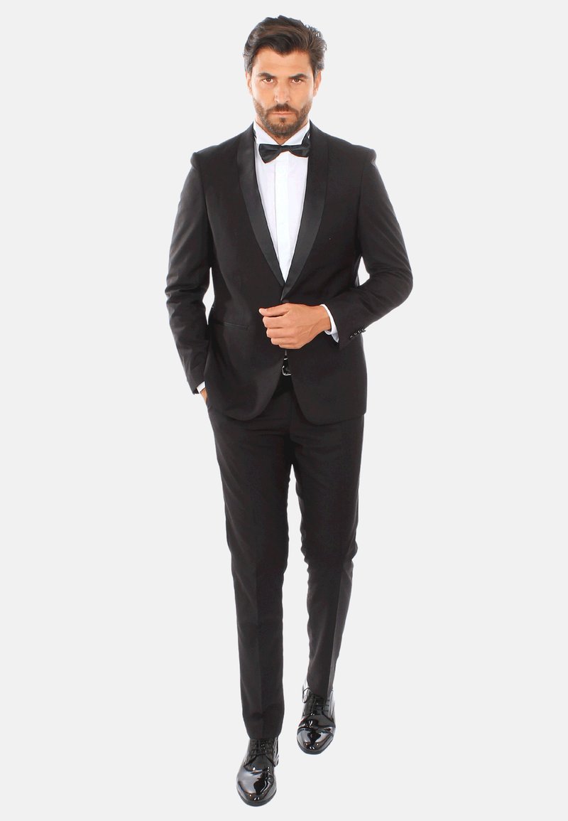 Tuxedo nero con rever in satin, camicia bianca e papillon nero. Design aderente, texture liscia, abbinato a scarpe classiche nere lucide.