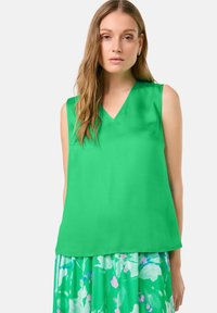 Sleeveless green blouse in smooth fabric with a V-neckline and loose fit, paired with a floral print skirt in shades of green and pink.