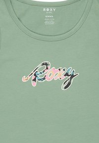 Grön ekologisk bomullstopp med en stor, flerfärgad "Roxy"-logotyp med blommiga detaljer. Rundad halsringning och mjuk textur.