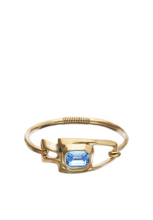 Bracelet en or conçu comme une épingle de sécurité avec une pierre précieuse bleue rectangulaire au centre, et un détail enroulé sur le bracelet.