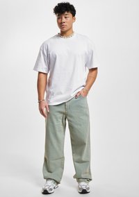 Camiseta de algodón blanca, de corte holgado. Pantalones vaqueros de pierna ancha en verde claro. Zapatillas en gris y negro con acentos. Collares y pulseras de cuentas como accesorios.