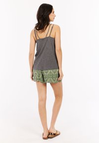 Un débardeur gris avec des bretelles fines, associé à un short vert avec un motif géométrique. Porté avec des sandales à lanières marron.