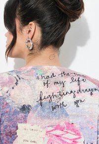Camisa ligera y multicolor con estampados florales y texto escrito a mano. Con un gráfico sutil debajo del cuello.