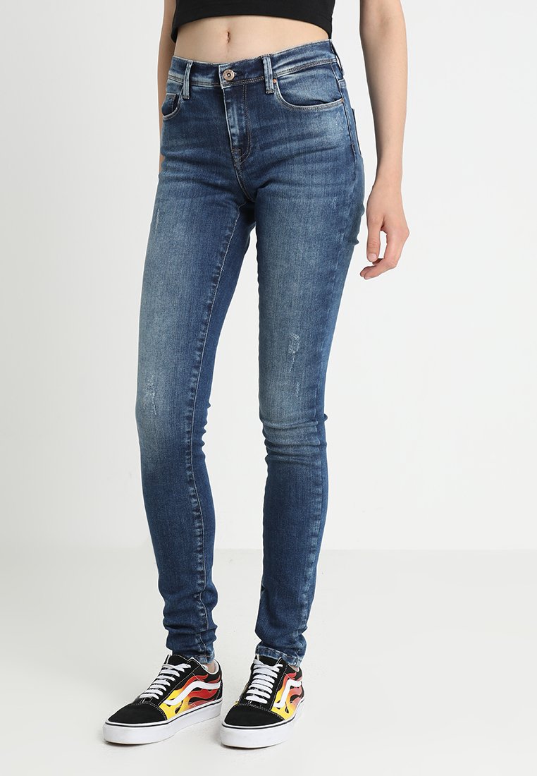 Blue skinny jeans made of denim, featuring a high waist, slight distressing, and front pockets. Paired with black sneakers with flame accents.