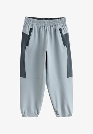 Heleroosad spordipüksid tumedate hallide küljeribade, elastse vöökohaga, tõmblukuga taskute ja elastsete sääristega pahkluude juures.