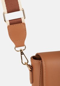 Coin de sac en cuir marron avec fermoir doré attaché à une large sangle en tissu rayé beige et marron.