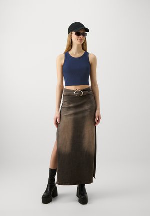 Navy geripptes Crop-Top, braße Jeans-Maxikleid mit seitlichem Schlitz, silberne kreisförmige Gürtelschnalle, schwarze Mütze, Sonnenbrille und klobige schwarze Plateaustiefel.