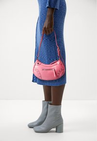 Rosa läderhandväska med böjd form, dragkedjeficka och nitar, kombinerad med grå stövletter med klack och en blå ribbstickad klänning.