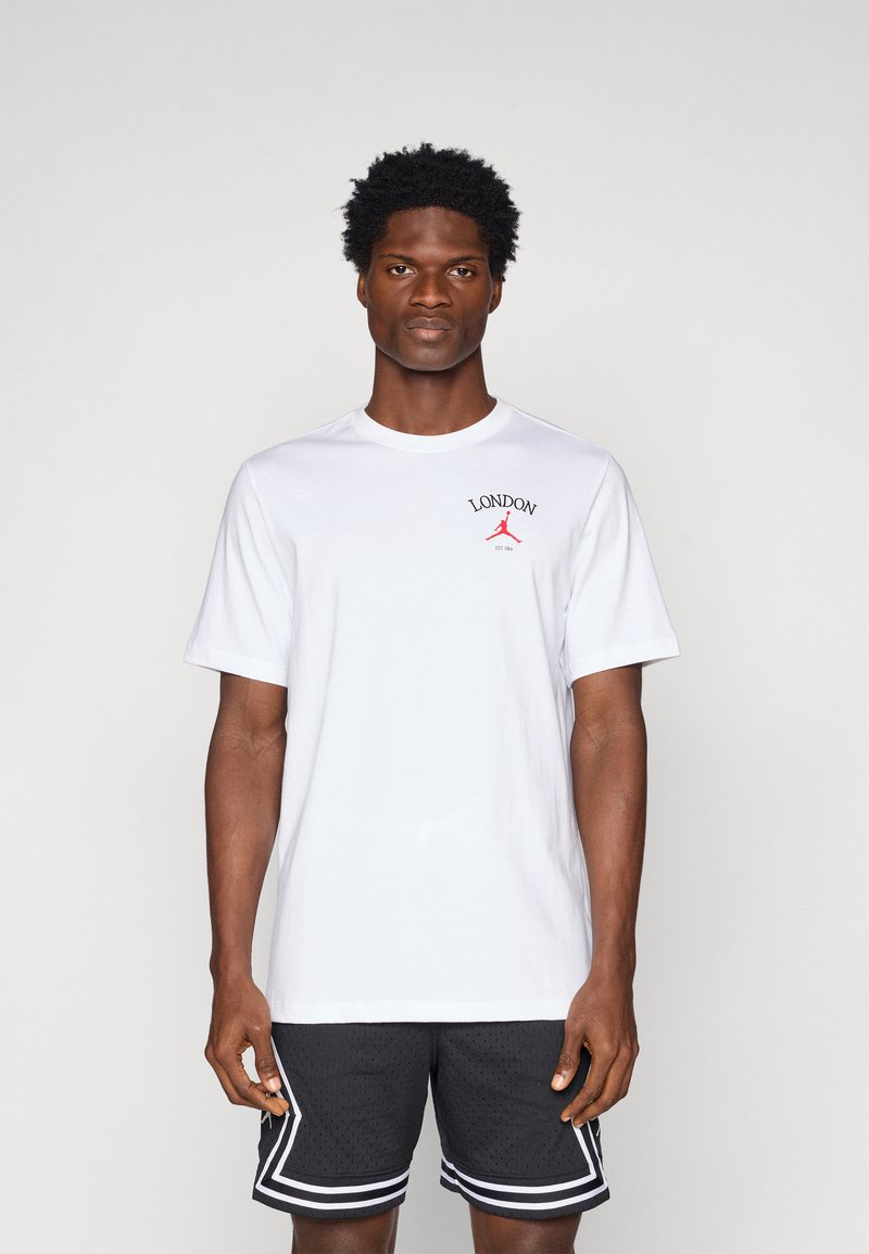 T-shirt en coton blanc avec l'inscription "LONDON" et un logo Jordan rouge sur la poitrine, associé à un short de sport en mesh noir avec des accents blancs.