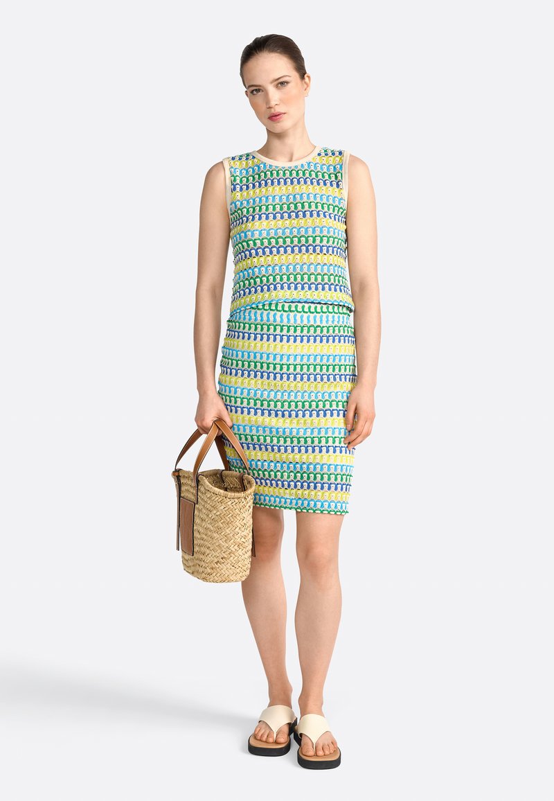 Färgglad ärmlös klänning med ett geometriskt mönster i blått, grönt och gult. Bärs med en flätad halmväska och ljusa sandaler.