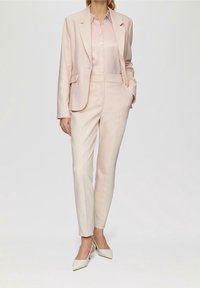 Completo su misura rosa chiaro con blazer a un petto e tasche frontali, abbinato a una blusa in satin e pantaloni a sigaretta. Completato con tacchi beige.