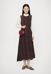 Abito lungo a quadri in rosso scuro e nero, con una camicia bianca sotto. Tiene una borsa a forma di cuore glitterata rossa. Scarpe con stampa leopardata.