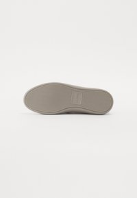 Talpă de pantof din cauciuc de culoare bej, cu un model de striație în zigzag și logo embosat. Textură netedă, cu margini rotunjite și detalii minime.