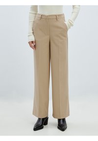 Beige gestreifte, hoch-taillierte Hose mit weitem Bein, ausgestattet mit zwei Seitentaschen und einer glatten Textur, kombiniert mit schwarzen Absatzstiefeln.