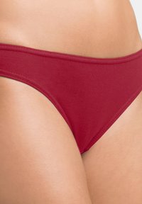 Bas de bikini en coton rouge avec une texture lisse, présentant un design taille basse et une ceinture élastique pour un ajustement confortable.