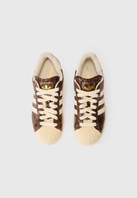 Tênis com estampa de cobra marrom e detalhes em creme, apresentando um design de três listras, bico clássico e sistema de cadarço. Detalhe de marcação em dourado visível.