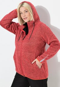 Veste en polaire rouge avec capuche, dotée d'une fermeture éclair à l'avant, de deux poches et d'accents orange contrastants. Tissu texturé avec un motif de tacheté.