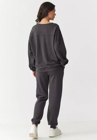 Szary sweatshirt i dopasowane dresy wykonane z miękkiego materiału, posiadające luźny krój i ściągacze. Noszone z białymi sneakersami.