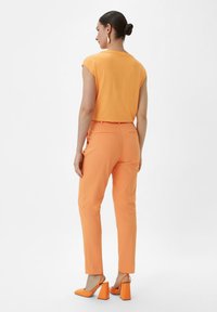 Oranges Kurzarmoberteil kombiniert mit orangen, schmal geschnittenen Hosen und orangen Blockabsatzschuhen, die eine glatte Textur und ein klares Design aufweisen.