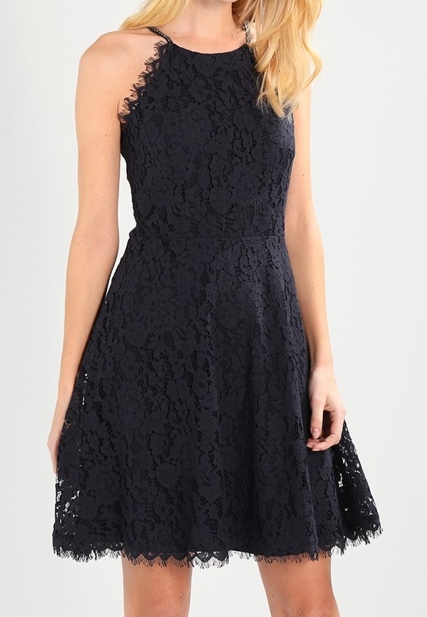 Robe noire en dentelle sans manches avec un col haut, une taille cintrée et une jupe évasée qui s'arrête au-dessus du genou.